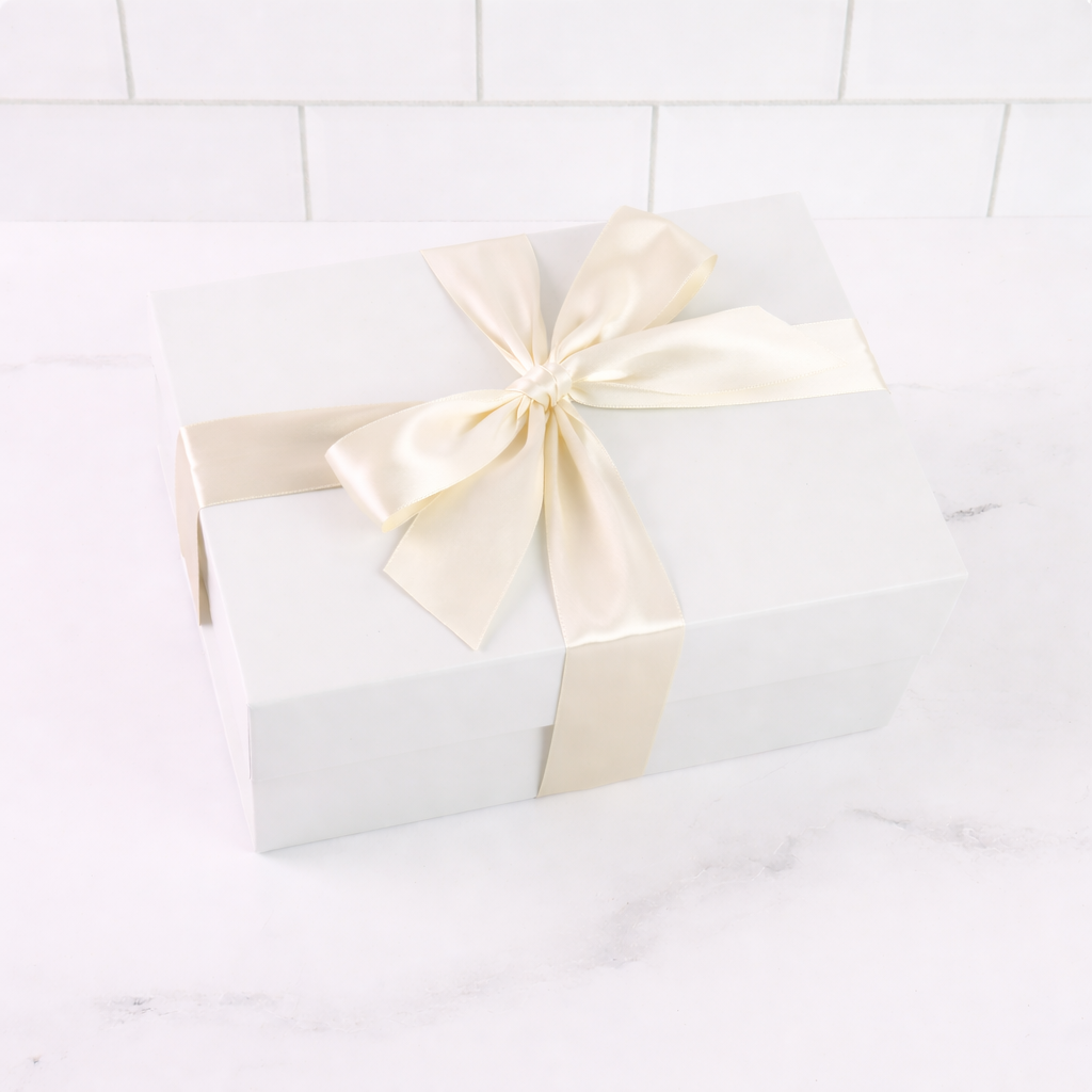 White gift box with a large cream ribbon on a white tiled background