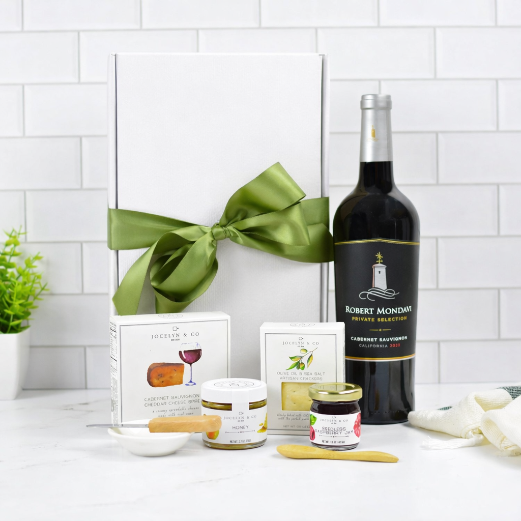 Wine bottle with a green ribbon, cheese, and crackers on a white surface with a tiled wall background.