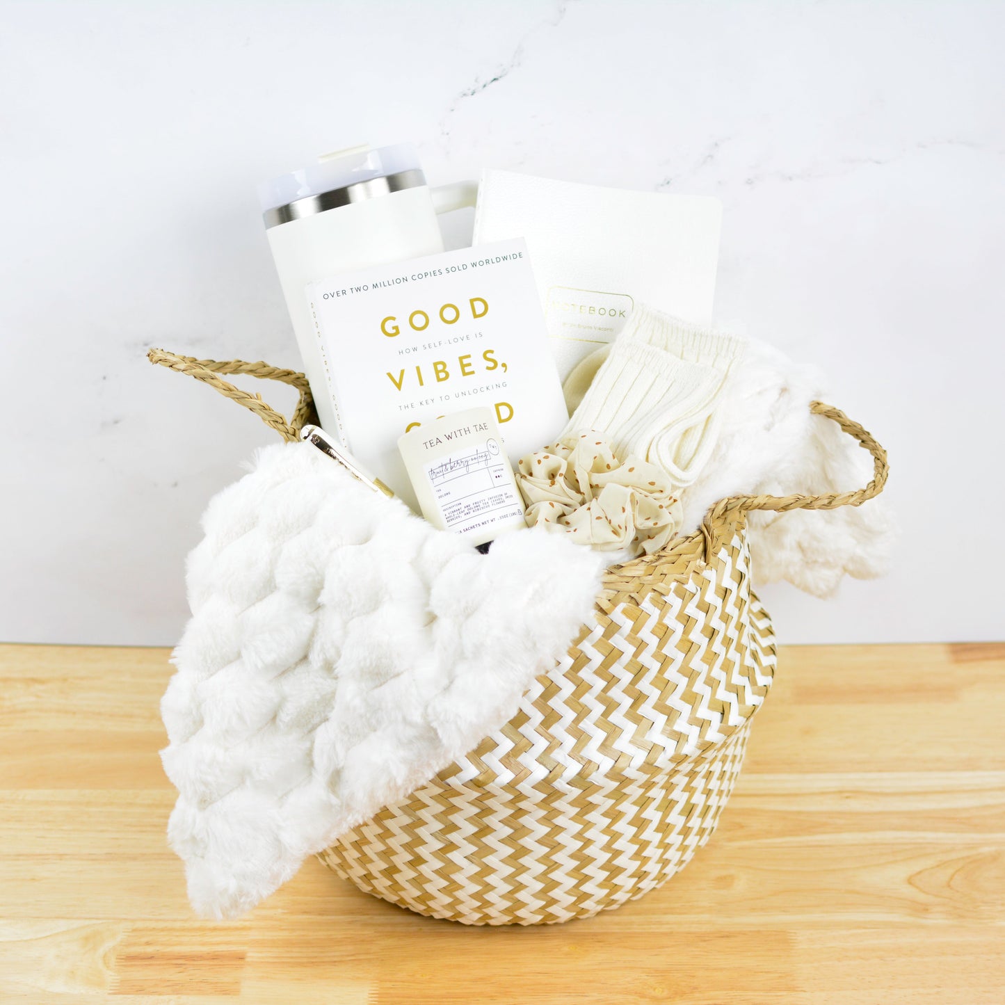 B.asket with a white blanket, tumbler, Good Vibes book, journal and candle